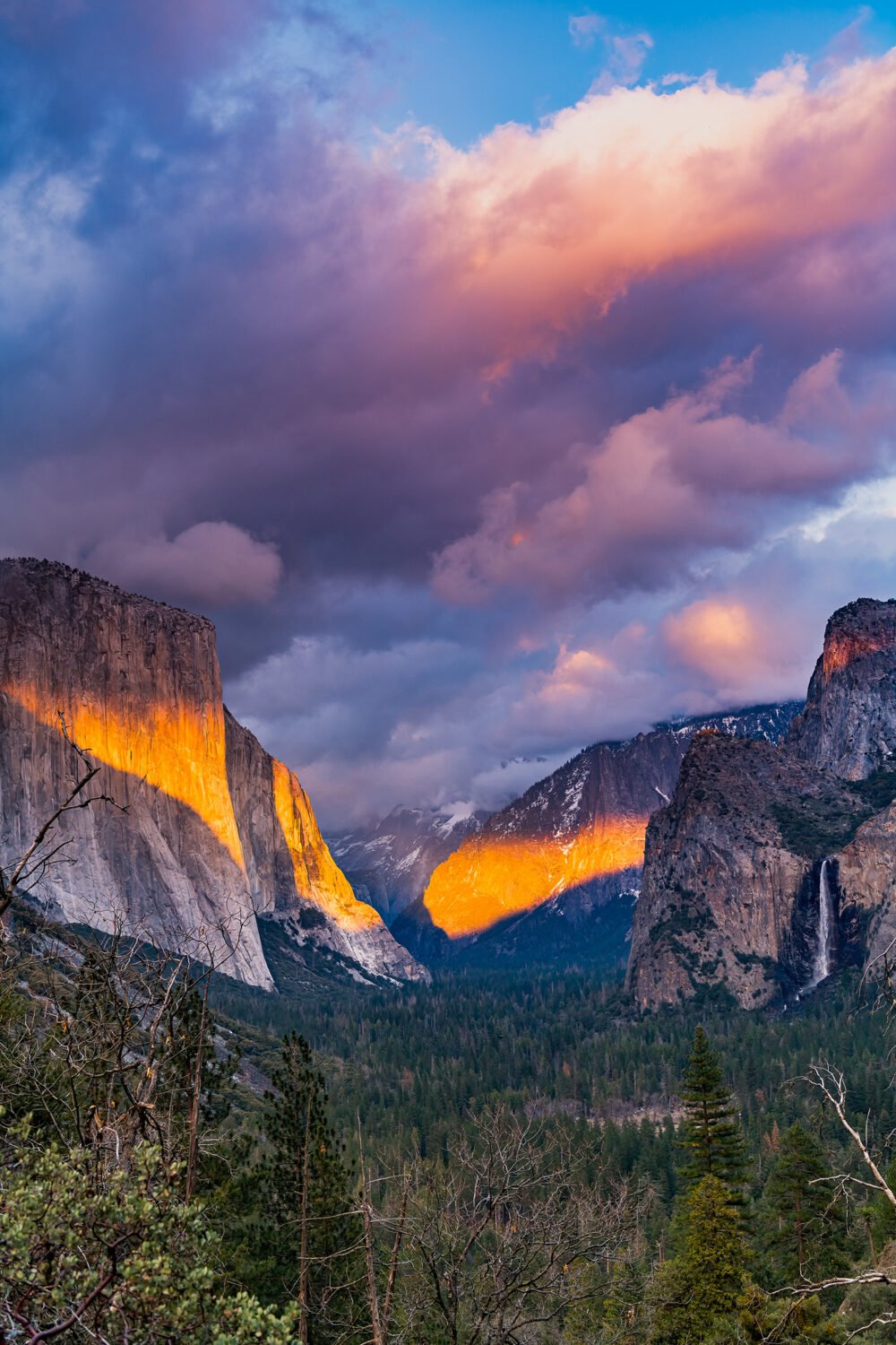 Sunset, as a storm approaches, highlights Firefall on El Capitan. Darkness falls over the rest of Yosemite Valley's forests, mountains, and waterfalls.