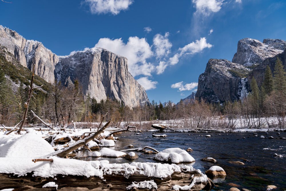 The snow covered and sparkling water of the Merced River framed by sheer cliffs, mountains and waterfalls as viewed from Yosemite Valley