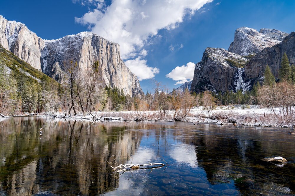 Sparkling water of the Merced River surrounded by a snowcapped mountains and frozen waterfalls as viewed from Yosemite Valley