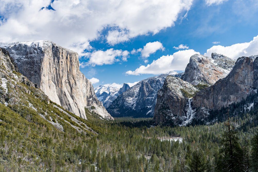 Puffy clouds and pristine weather highlight the beauty of nature in dramatic mountains, frozen waterfalls and forests dusted in snow in Yosemite