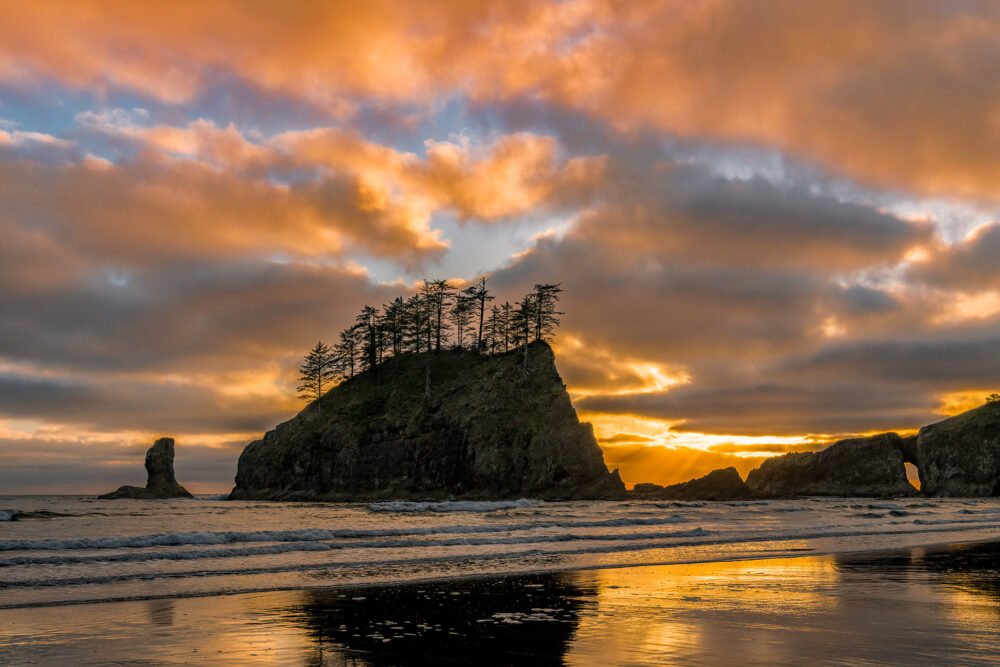 Beautiful and colorful clouds at sunset behind sea stacks reflect in the Pacific Ocean at Second Beach on the Washington Coast.