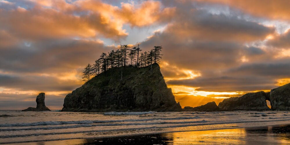 Beautiful and colorful clouds at sunset behind sea stacks reflect in the water in this panorama at Second Beach on the Washington Coast.
