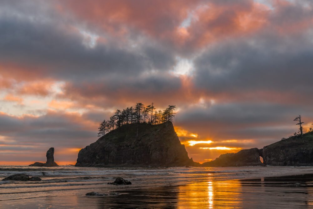 A beautiful and colorful sunset behind sea stacks reflects in the Pacific Ocean at Second Beach on the Washington Coast.