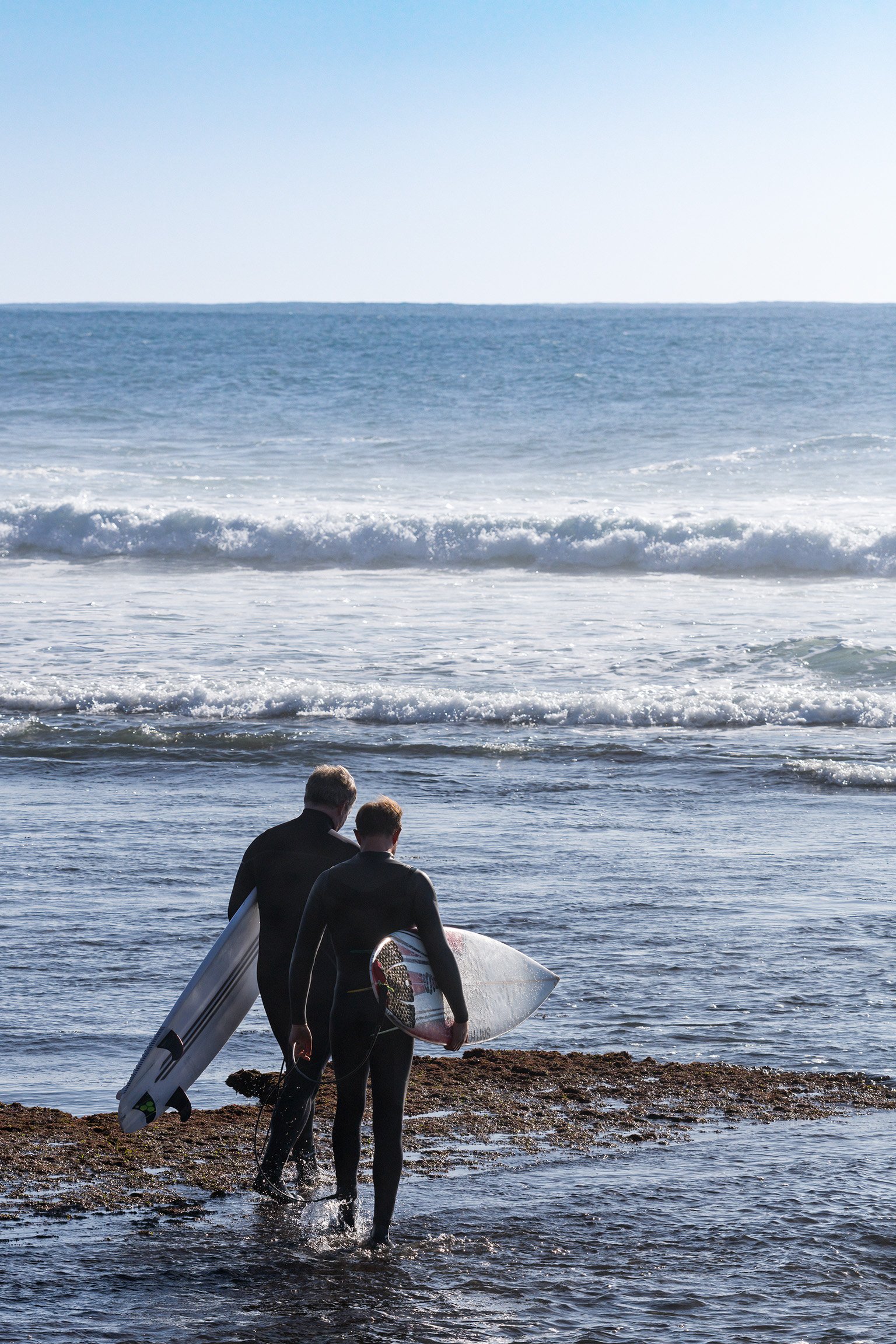 Two buddies head towards the waves for a day of surfing at Swami's Beach on the California Coast