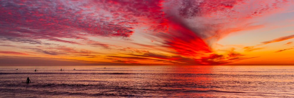Watching a brilliant and colorful sunset while surfing along the California coast - panorama