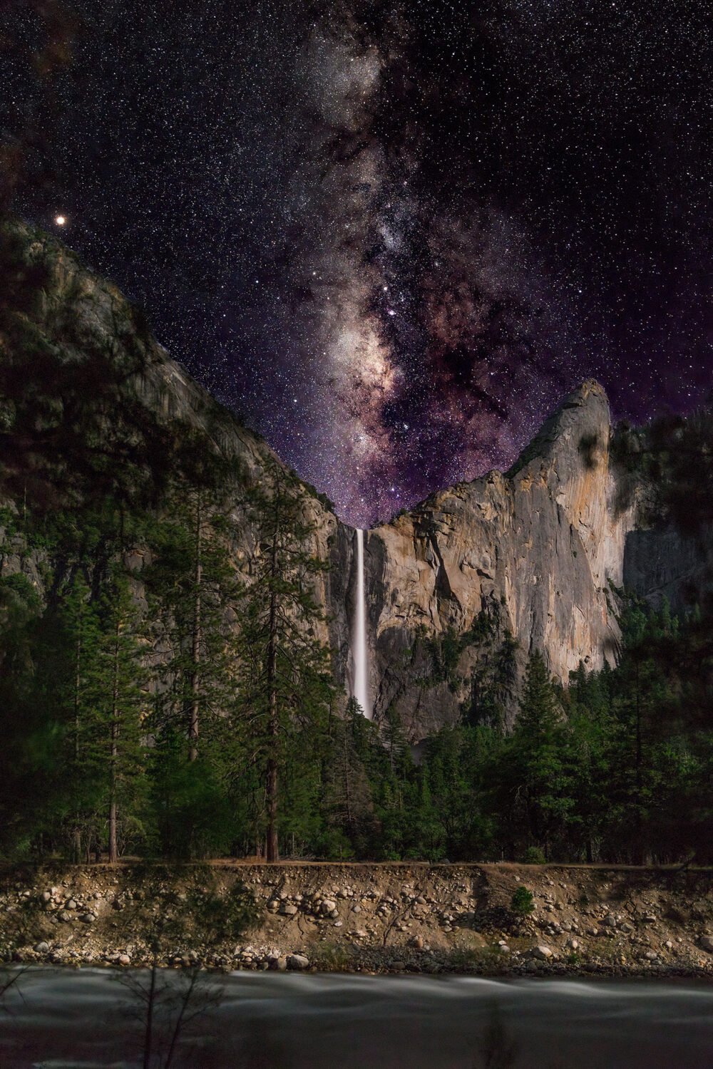 Moonlit Bridalveil Fall cascading off of the mountains in Yosemite Valley with the Merced River and The Milky Way lighting the sky