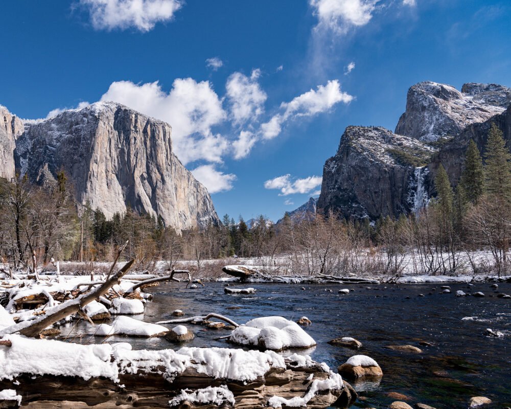 The snow covered and sparkling water of the Merced River viewed from Yosemite Valley and framed by sheer cliffs, mountains and waterfalls.